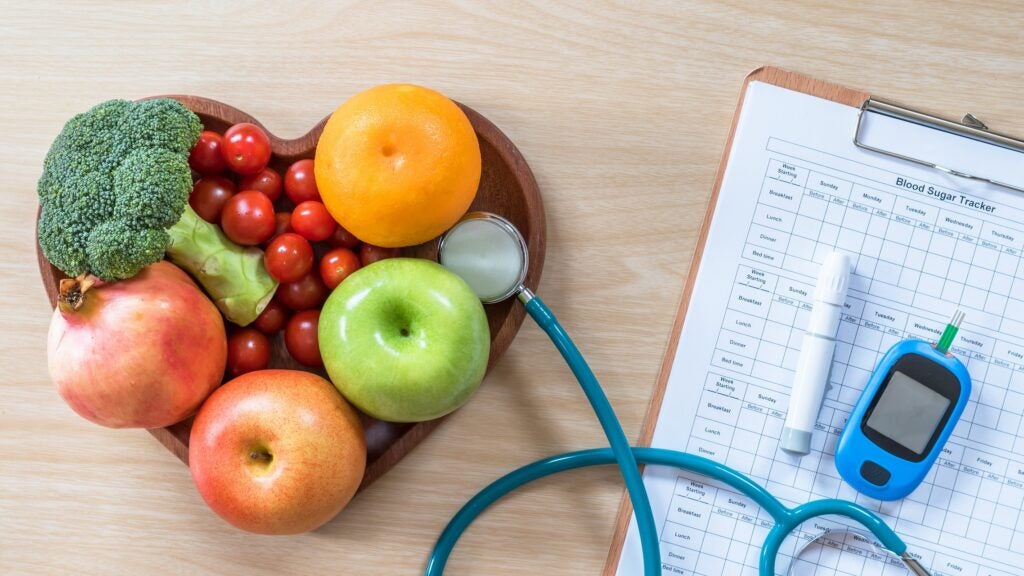 Diabetes monitor, clipboard, stethoscope, and a heart shaped bowl of healthy fruits and vegetables