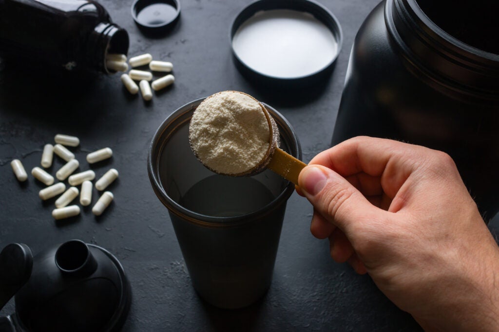 person making a workout shake including protein powder or another exercise supplement; exercise supplement capsules on table in background